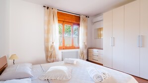 Quarto de hotel com cama, mesa de cabeceira, penteadeira, espelho e janela com cortinas.