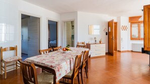 Uma sala de jantar com uma mesa posta para quatro pessoas, rodeada por cadeiras de madeira. Há um lustre sobre a mesa.
