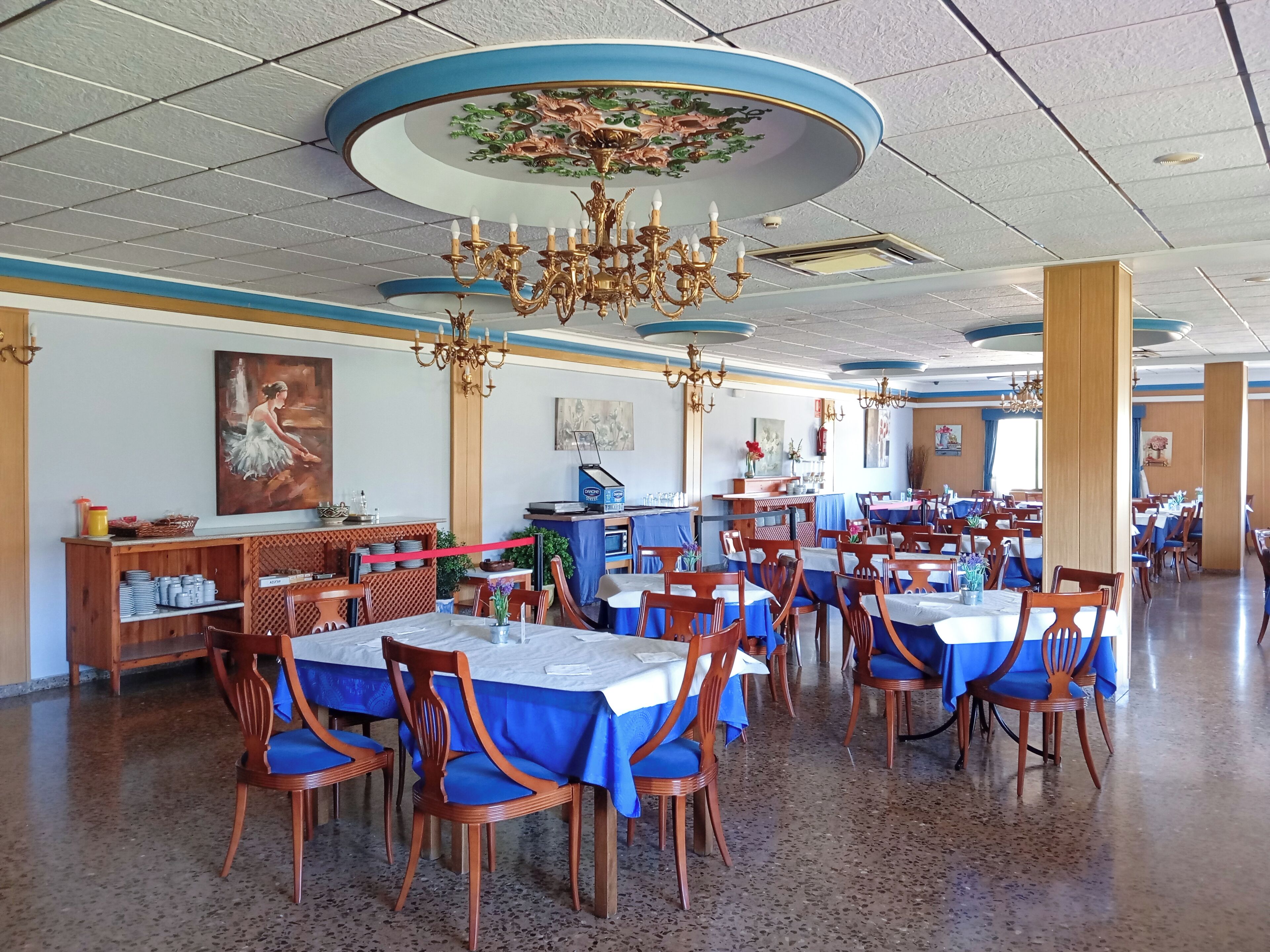 Un restaurante espacioso con varias mesas y sillas, un techo con candelabros decorativos y obras de arte en las paredes.
