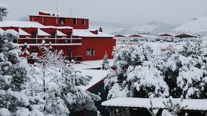 Un bâtiment rouge doté de nombreuses fenêtres et de balcons, entouré d’arbres couverts de neige et d’un paysage hivernal.
