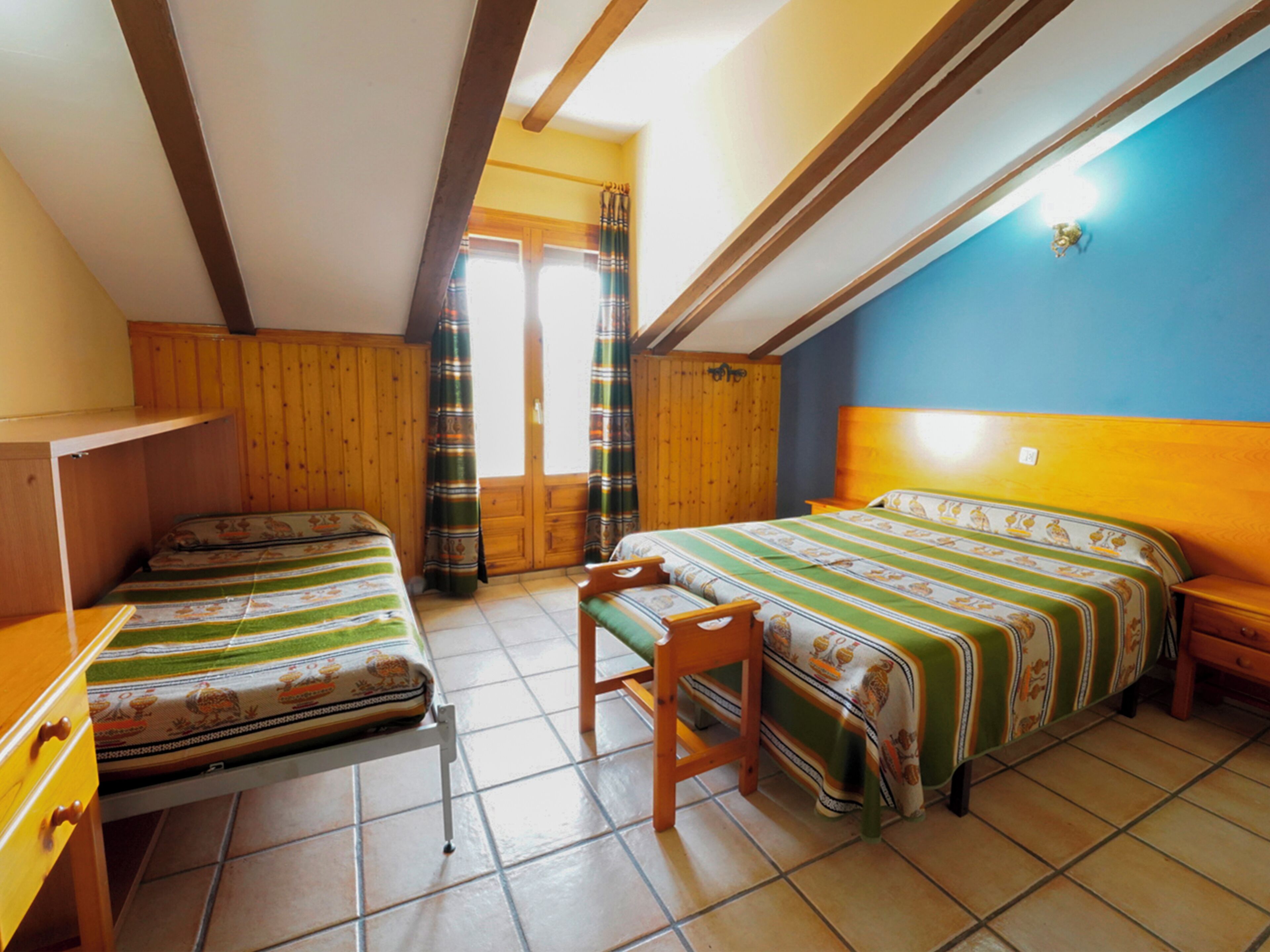A room with two beds, a wooden desk, and a chair.