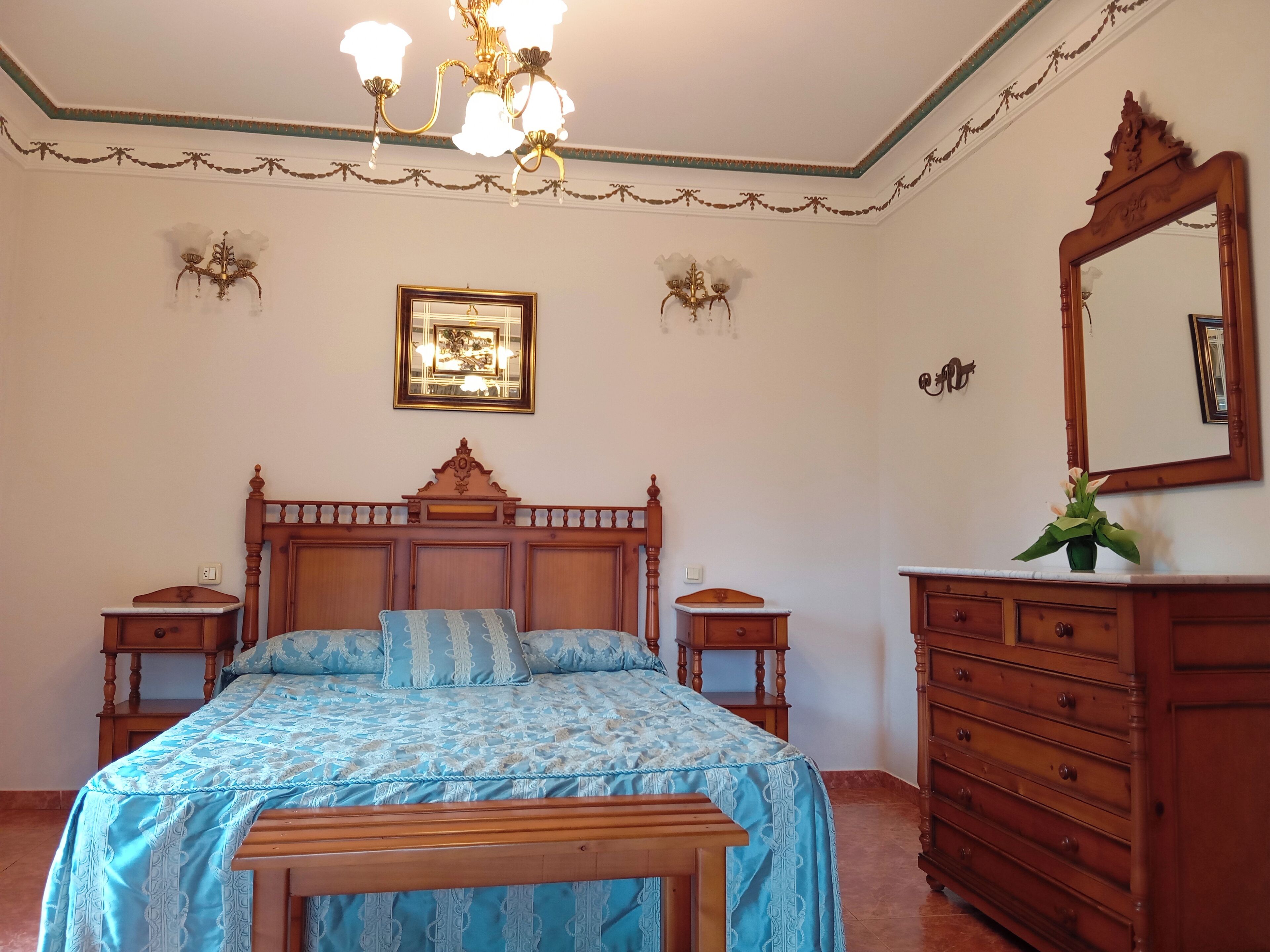 A bedroom with a wooden bed, a dresser, a mirror, and wall sconces.