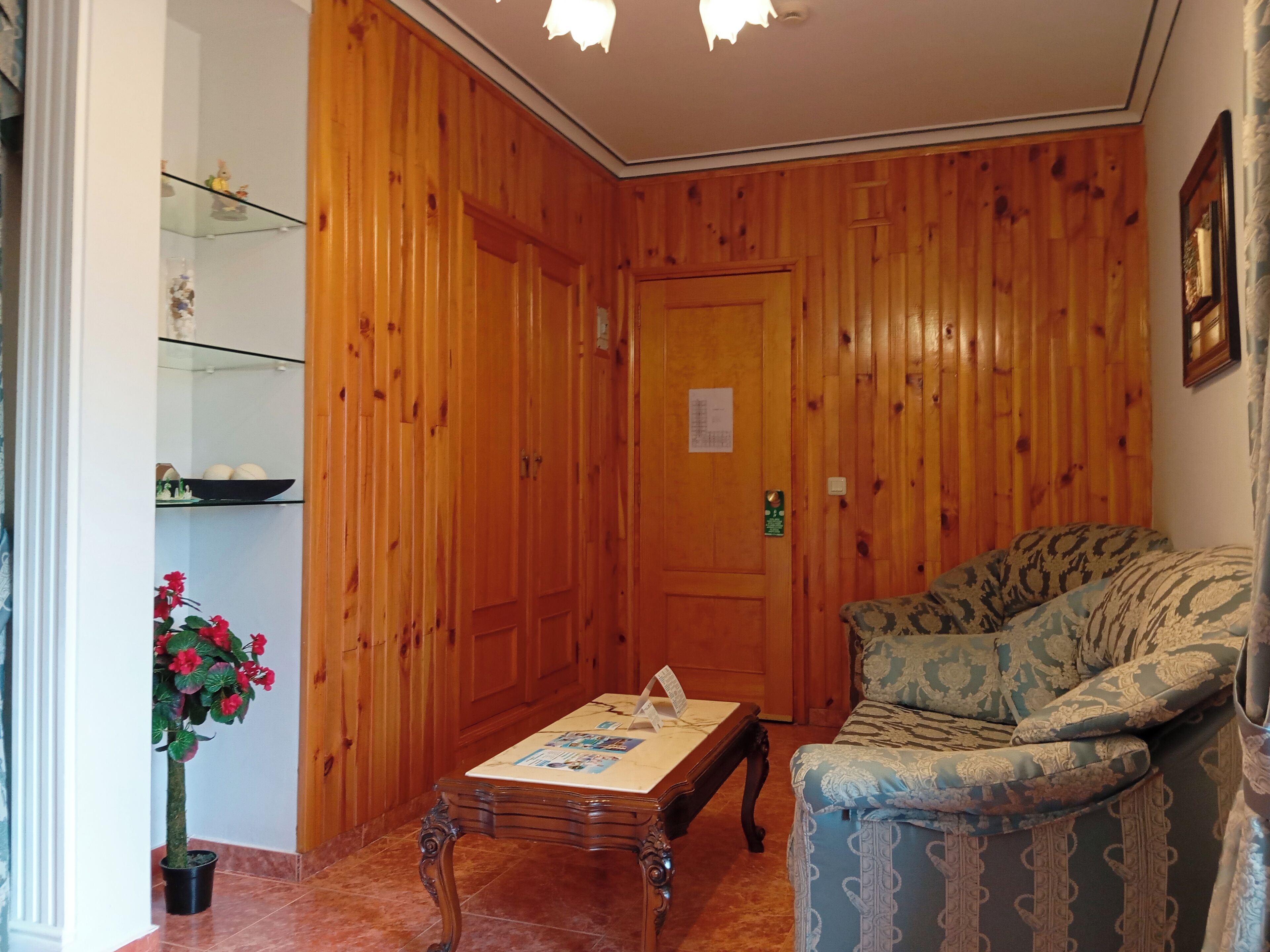 A wooden-paneled room with a sofa, a small table, and a potted plant.