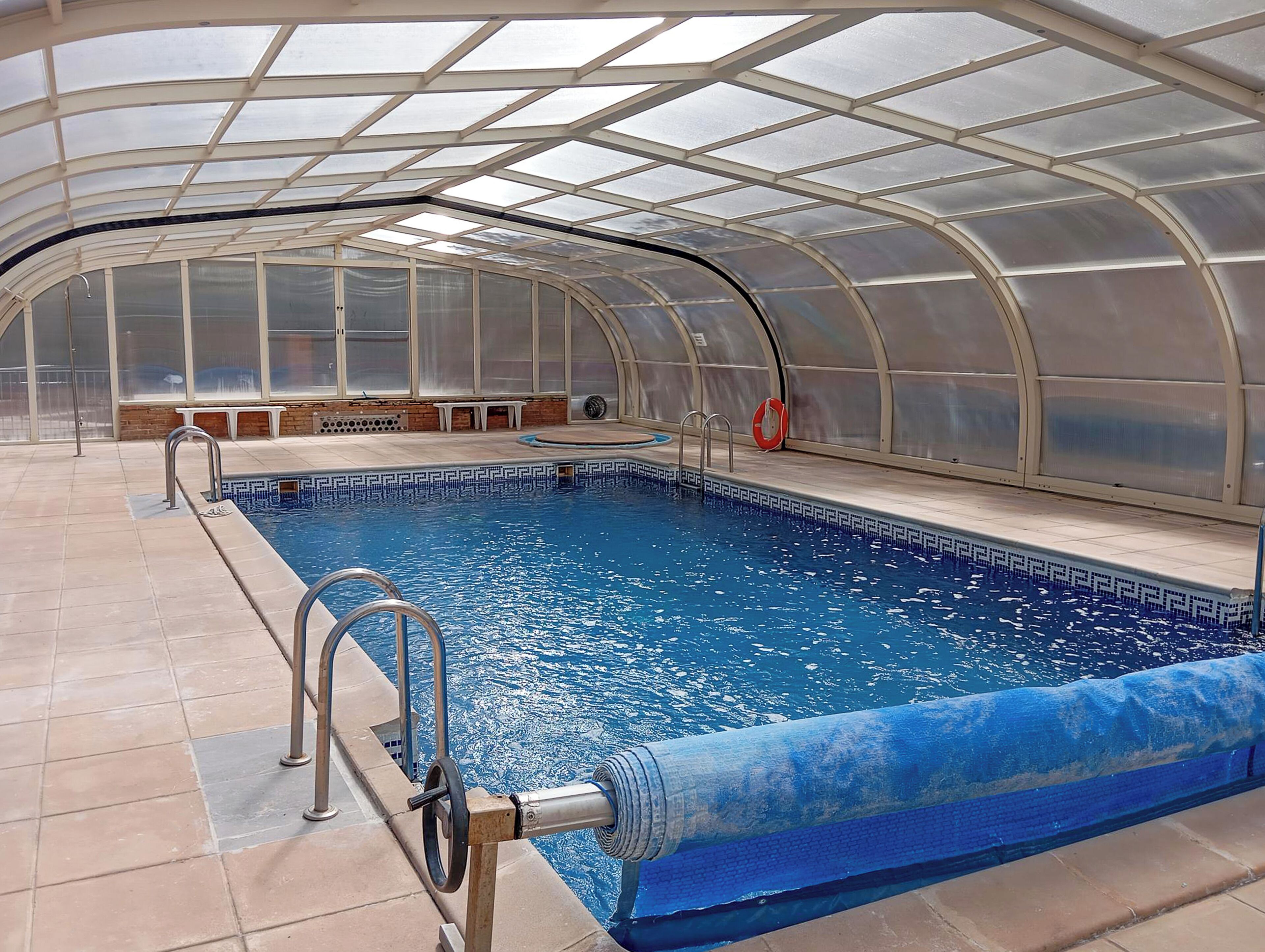 An indoor swimming pool with a glass ceiling, tiled floor, and a lifebuoy near the pool.