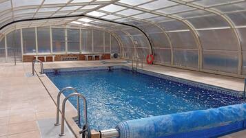 An indoor swimming pool with a glass ceiling, tiled floor, and a lifebuoy near the pool.