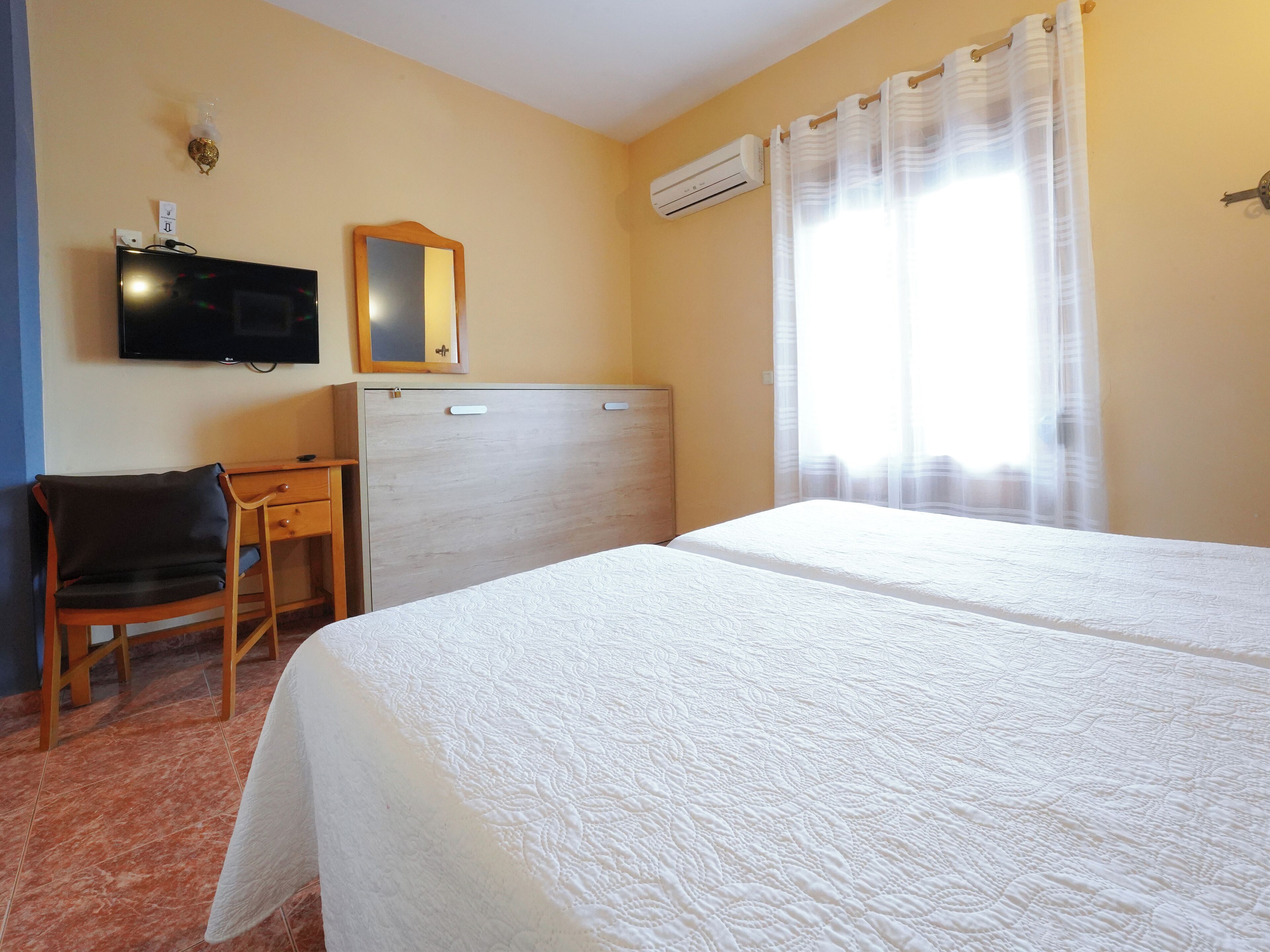 Una habitación de hotel con cama, escritorio, silla, televisión y aire acondicionado.