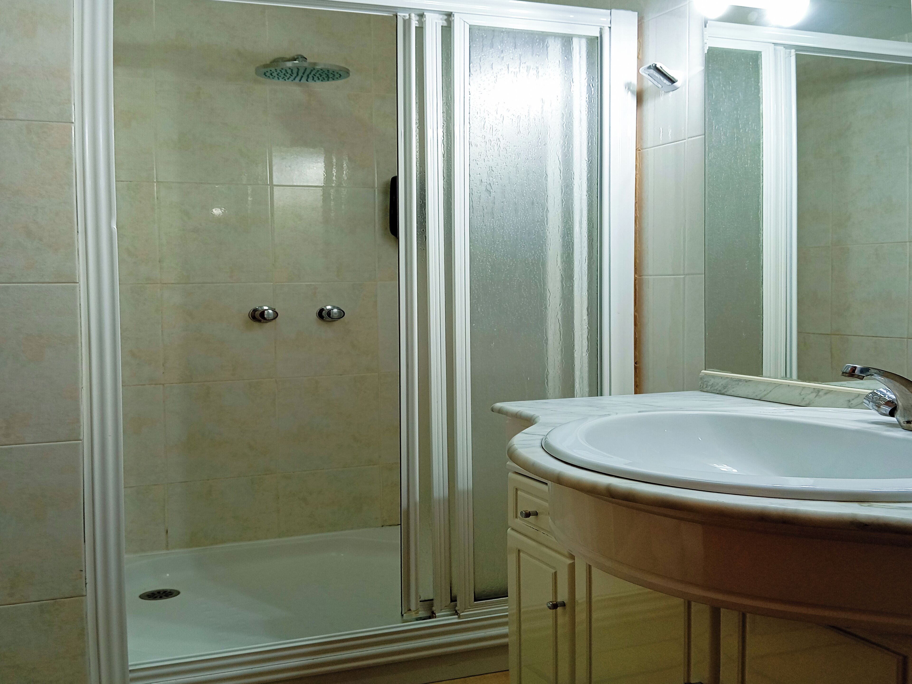 A bathroom with a glass-enclosed shower, a white sink, and a mirror.