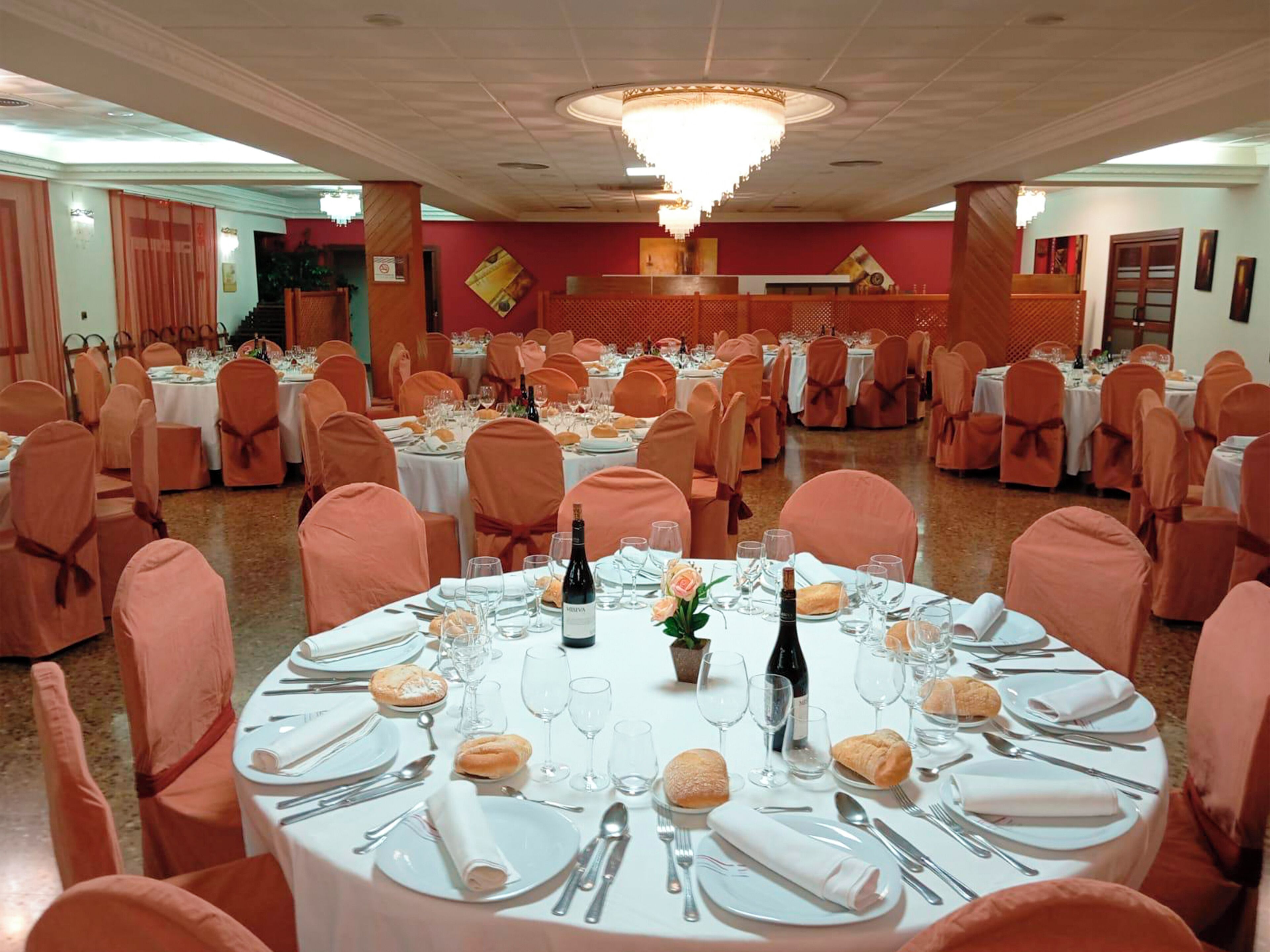 A banquet hall with round tables set for a formal event, featuring white tablecloths, neatly folded napkins, and a variety of tableware.