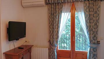 Una habitación con una televisión sobre un escritorio de madera, una ventana con cortinas estampadas y un equipo de aire acondicionado en la pared.