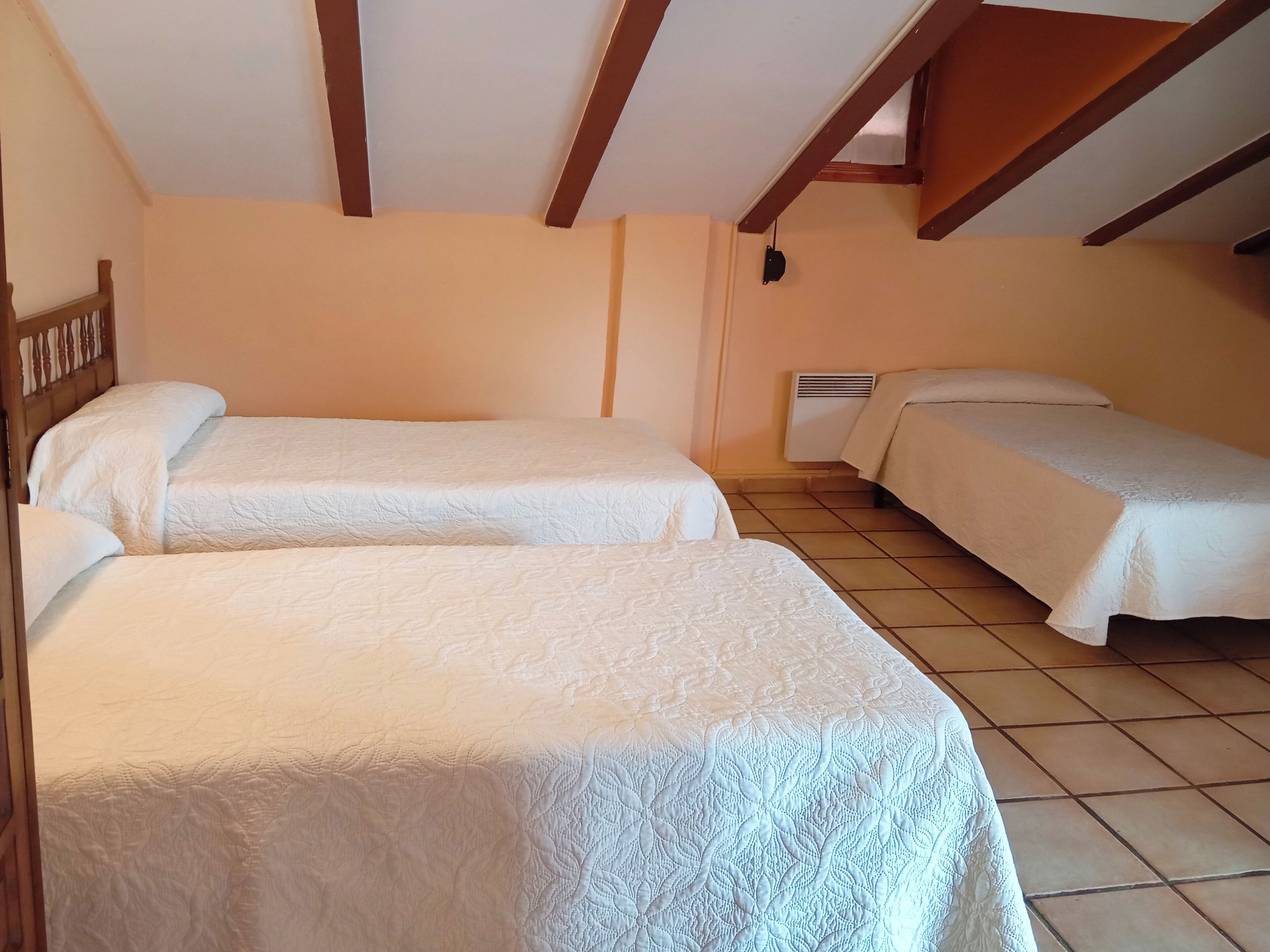 A room with two beds, wooden beams on the ceiling, and a wall-mounted heater.