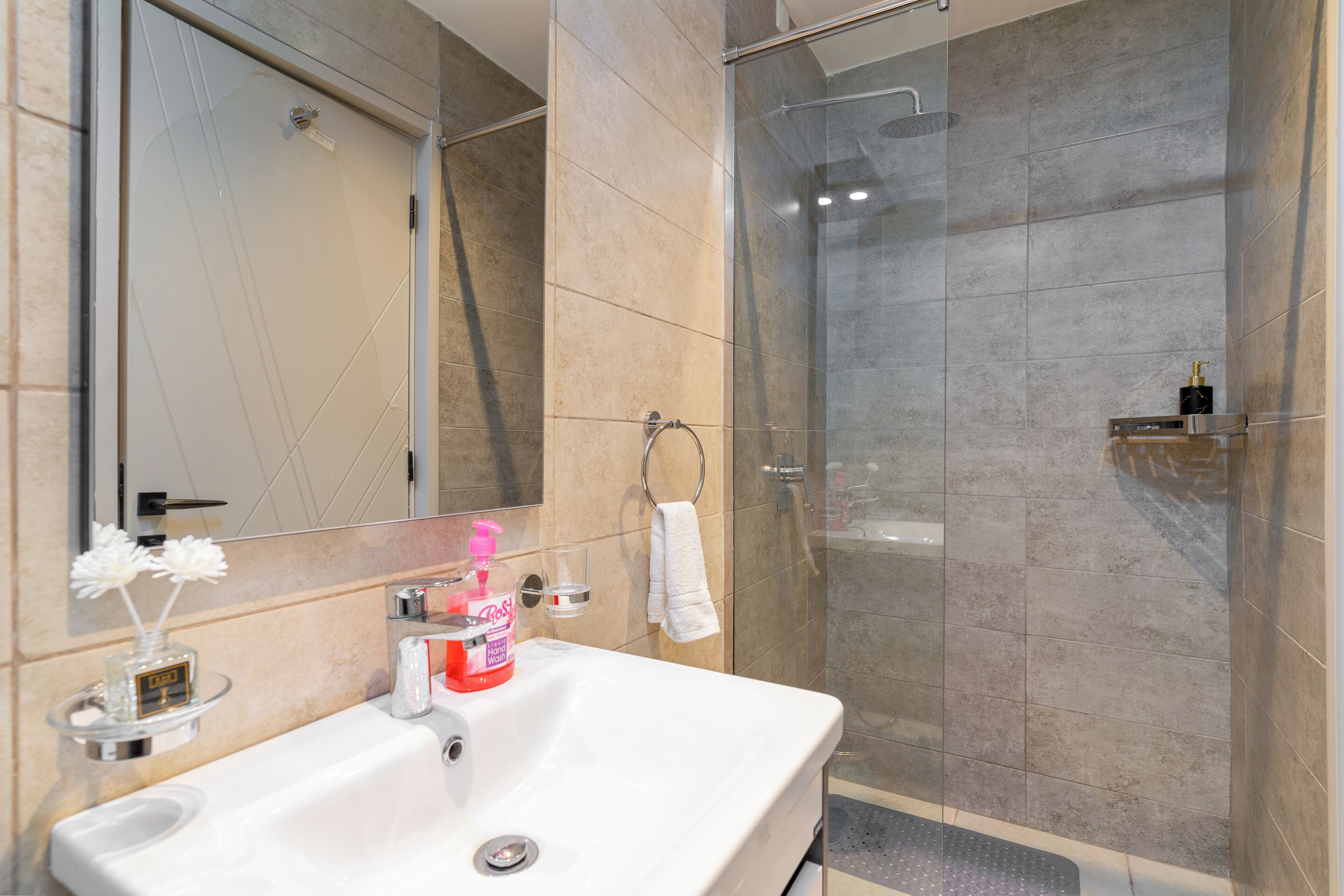 A bathroom with a white sink, a mirror, a glass shower enclosure, and a towel rack.