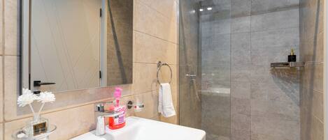A bathroom with a white sink, a mirror, a glass shower enclosure, and a towel rack.