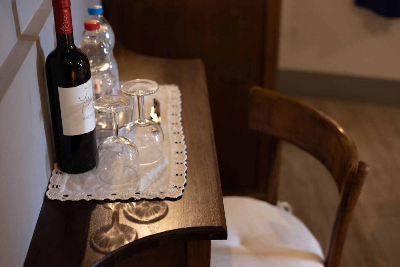 A table with a bottle of wine, two wine glasses, and a bottle of water on a lace doily.