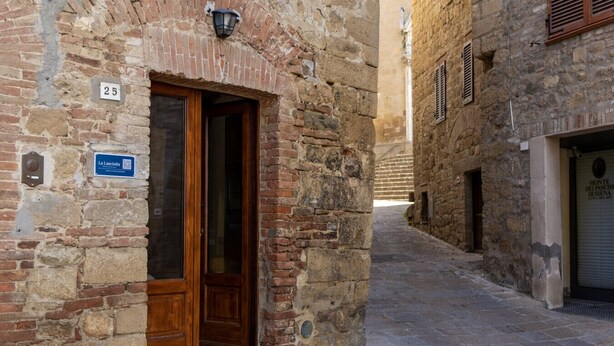 A narrow stone alley with a wooden door and a sign indicating a location. - Camera Lanciotta - Monticchiello (Monticchiello)