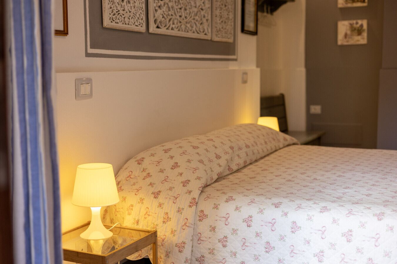 A neatly made bed with a floral-patterned bedspread and a bedside lamp.