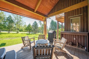 A wooden deck with outdoor seating and a grill, overlooking a grassy area with trees. - New! Ski In/Ski Out Home w/ Hot Tub & Fireplace (McHenry)
