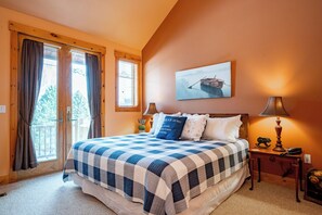 A bedroom with a large bed, a wooden headboard, a nightstand with a lamp, and a window with curtains. - New! Ski In/Ski Out Home w/ Hot Tub & Fireplace (McHenry)