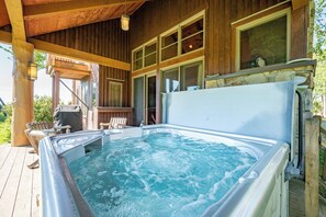 Een hottub in een houten chalet met terras en buitenmeubels.