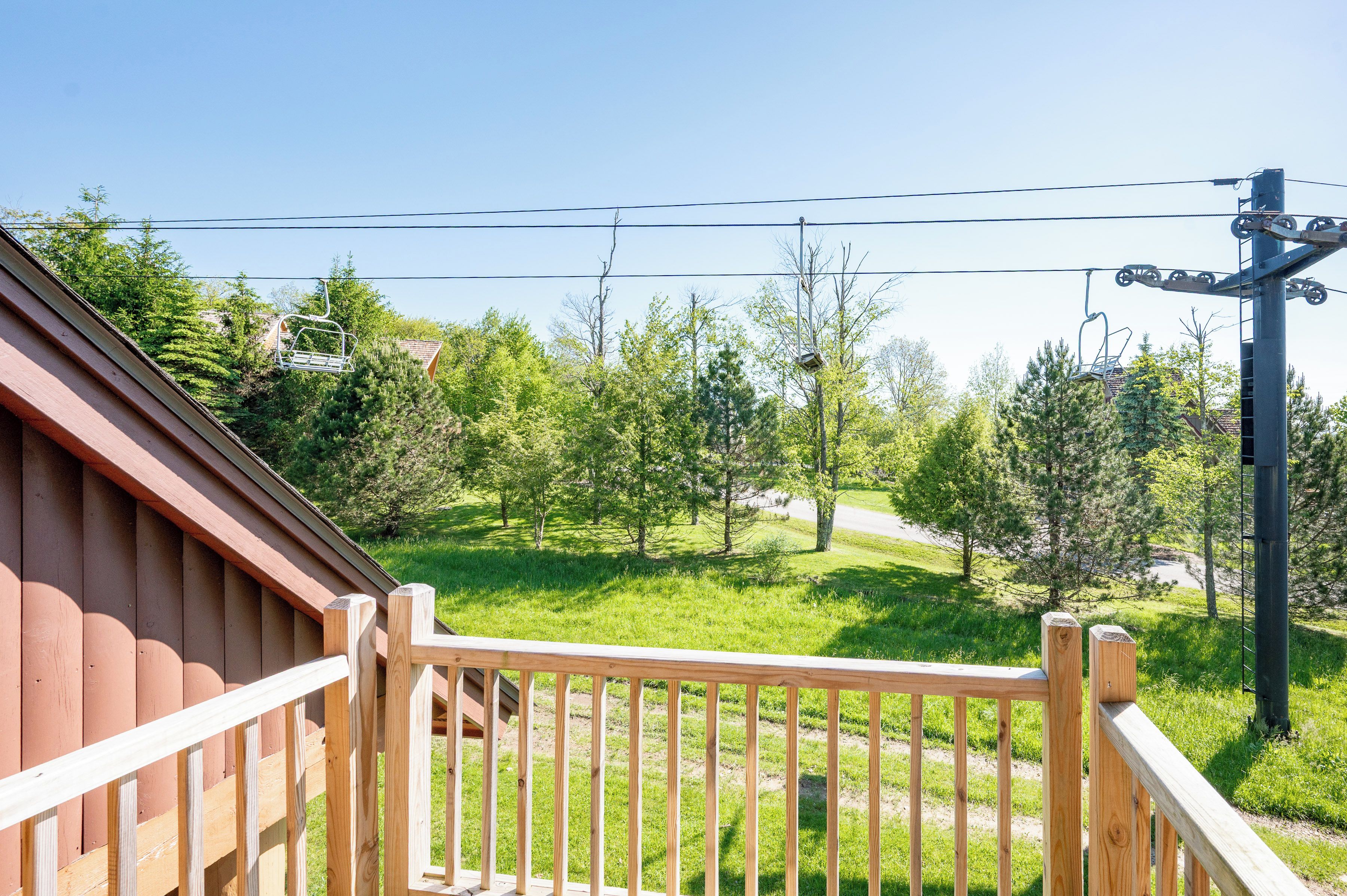 A wooden deck with a metal railing overlooking a grassy area with trees and a clear sky.