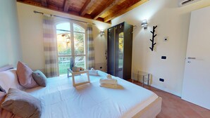 A bedroom with a large bed, a window with curtains, a door, and a wall-mounted light fixture. - Borgo Torchio F1 By Bookinggardalake (Manerba del Garda)