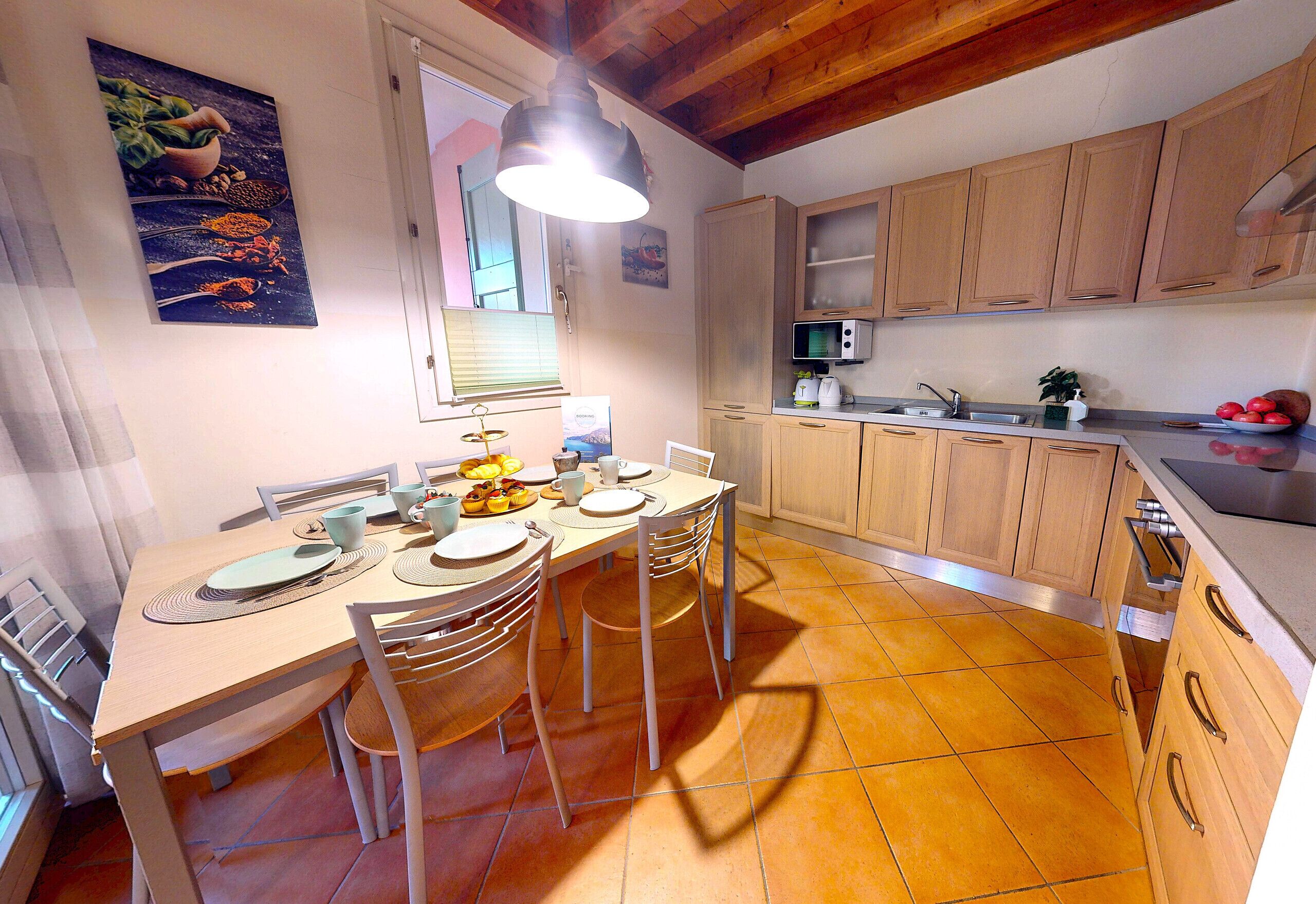 A kitchen with wooden cabinets, a dining table with chairs, a hanging light fixture, and a window with blinds.