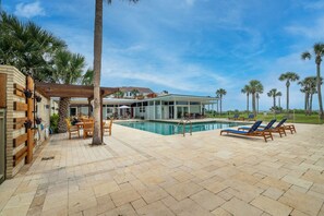 A pool area with lounge chairs, a pergola, and a view of a house with a pool.