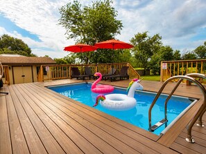 Une piscine avec une terrasse en bois, des chaises longues et des jeux gonflables.