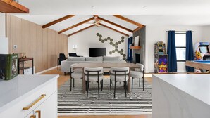 Un salon moderne comprenant un canapé, une table à manger avec des chaises, un téléviseur et un mur décoré de motifs hexagonaux.