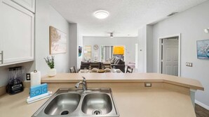 A modern kitchen with a double sink, a countertop, and a dining area in the background. - Lakefront Terra Verde Retreat Near Disney (Kissimmee)