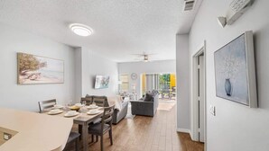 A modern living room with a dining area, a sofa, a TV, and a painting on the wall. - Lakefront Terra Verde Retreat Near Disney (Kissimmee)