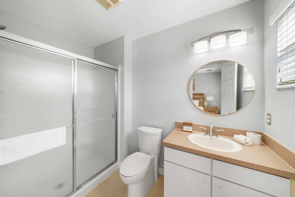 A bathroom with a glass shower enclosure, a toilet, a sink with a mirror, and a light fixture above the mirror.