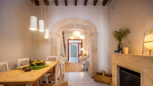 A dining area with a wooden table, chairs, hanging lights, a fireplace, and a hallway leading to a bedroom. - Ca'n Ruquet – Your Mallorcan Hideaway in the Heart of Campanet (Campanet)