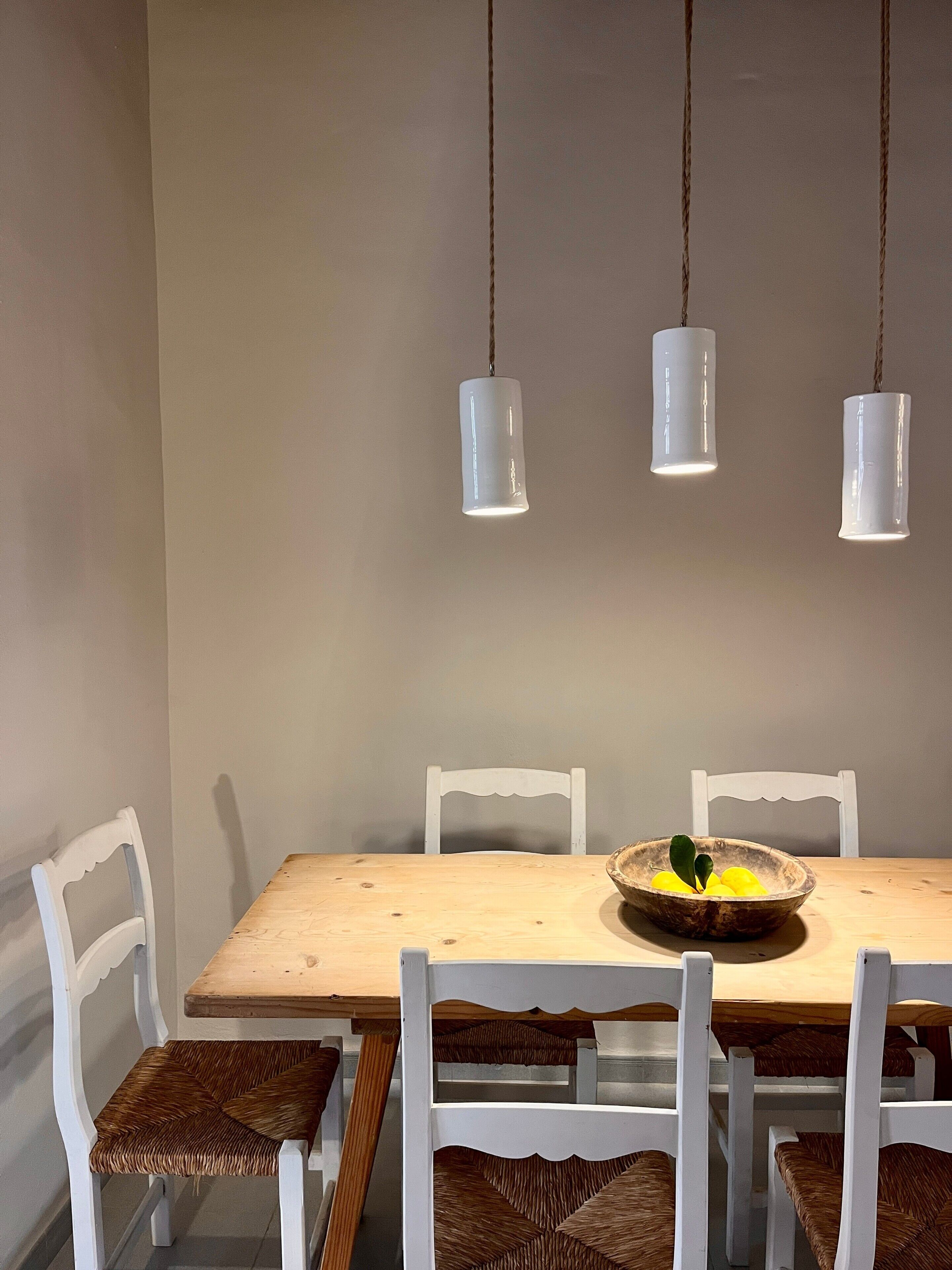 Un espace repas avec une table en bois, des chaises blanches et des lampes suspendues.