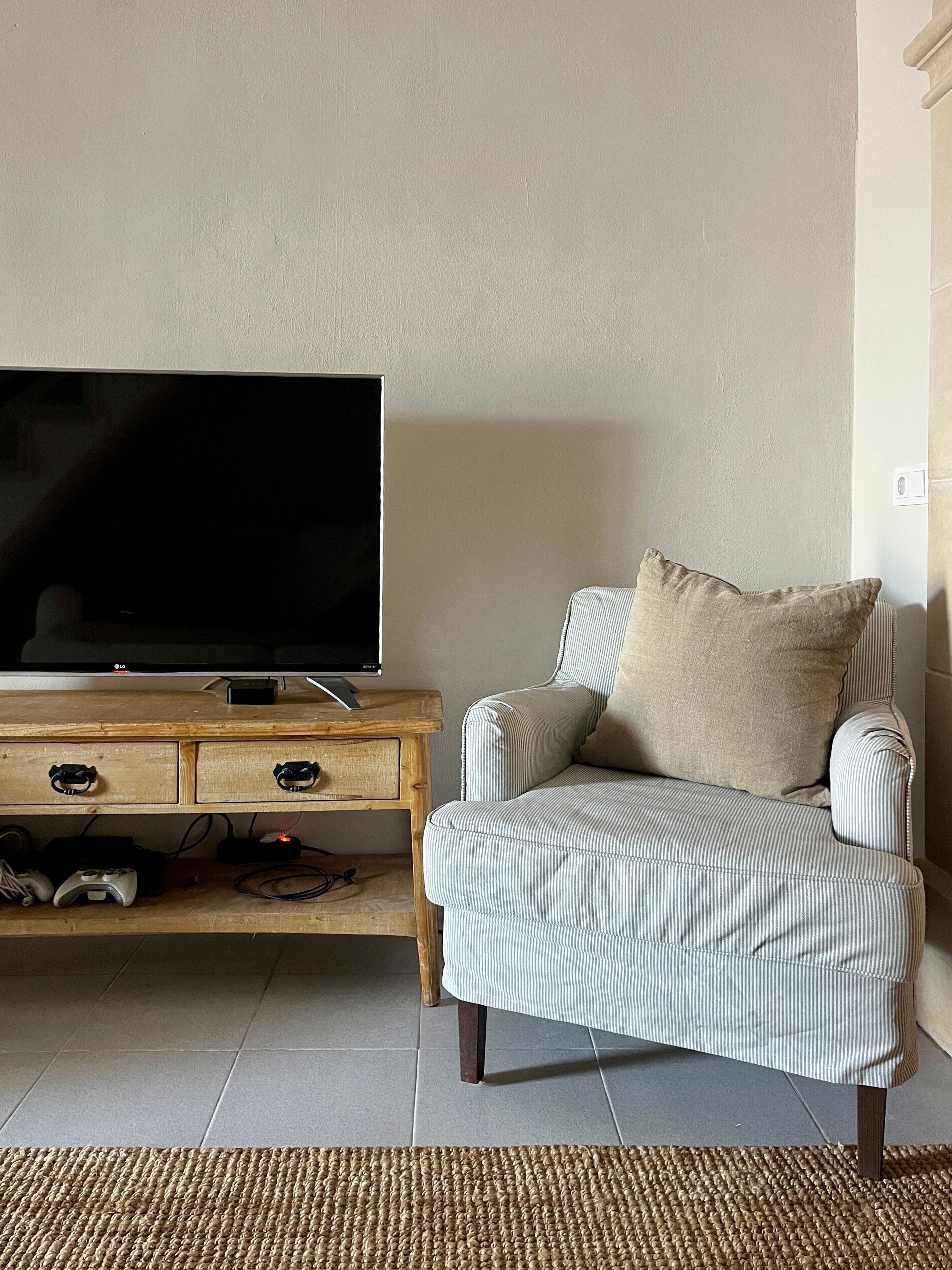 Un salon avec un téléviseur posé sur un meuble en bois, un fauteuil à rayures et un tapis tissé.