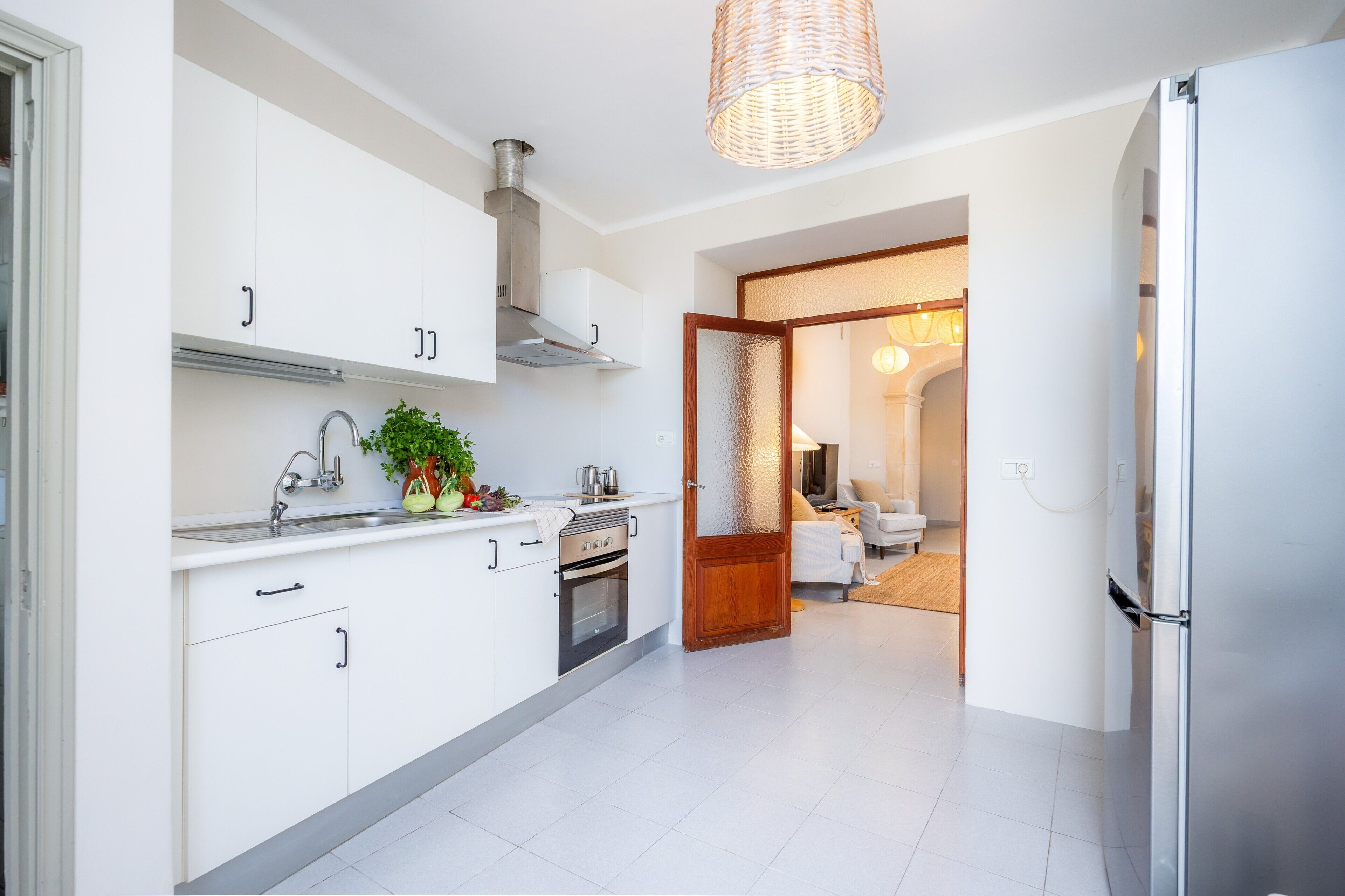 Una cocina moderna con armarios blancos, una campana extractora de acero inoxidable y una lámpara colgante.
