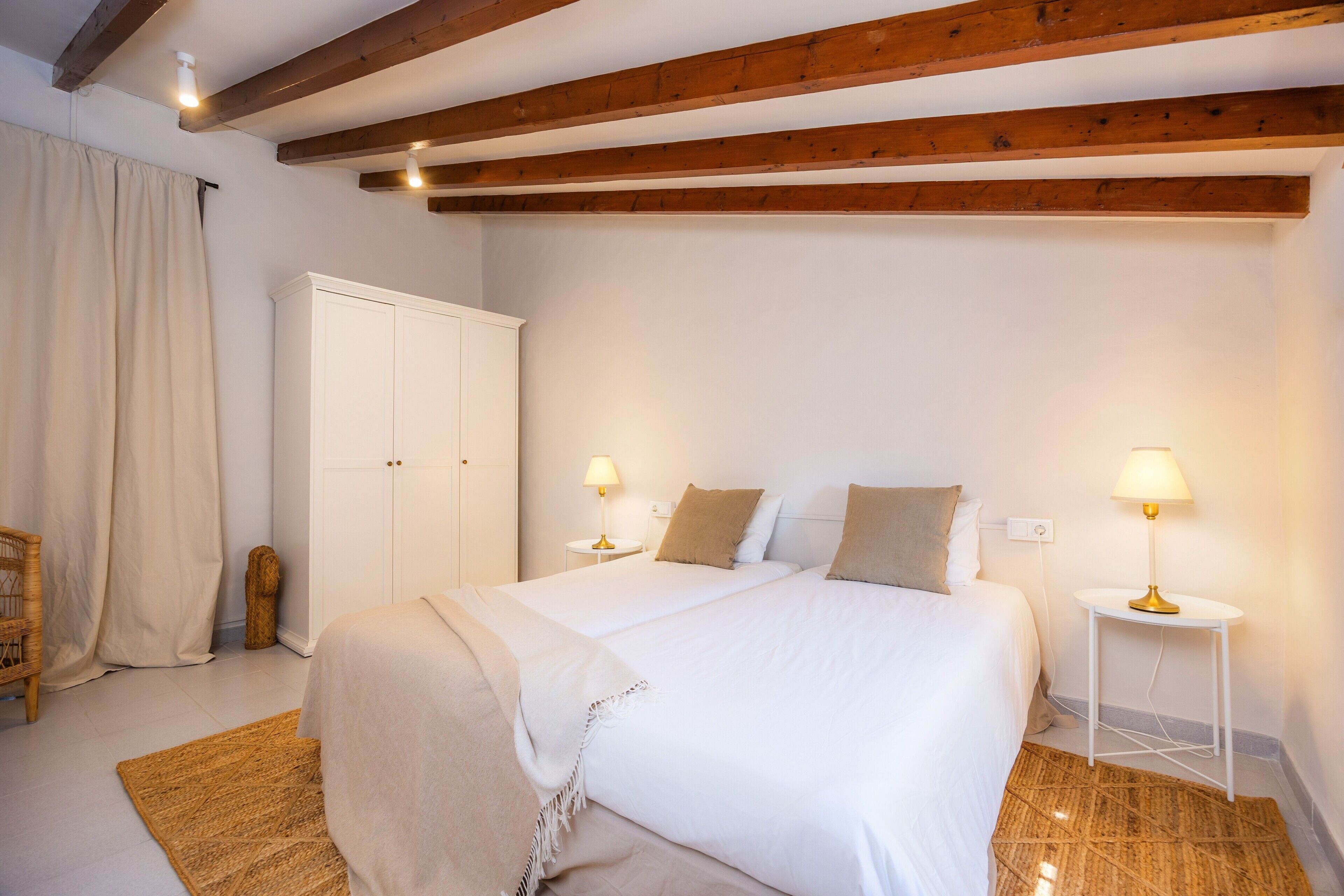 Ein Schlafzimmer mit einem großen Bett, zwei Nachttischen mit Lampen, einem Kleiderschrank, einem Sessel und einem Teppich.