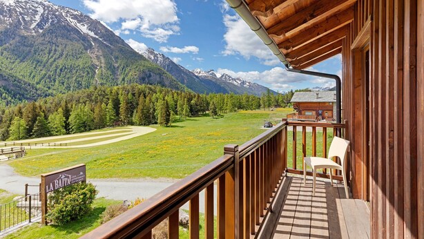 Un balcón de madera con vistas a un paisaje montañoso, un letrero que indica un restaurante y una silla.