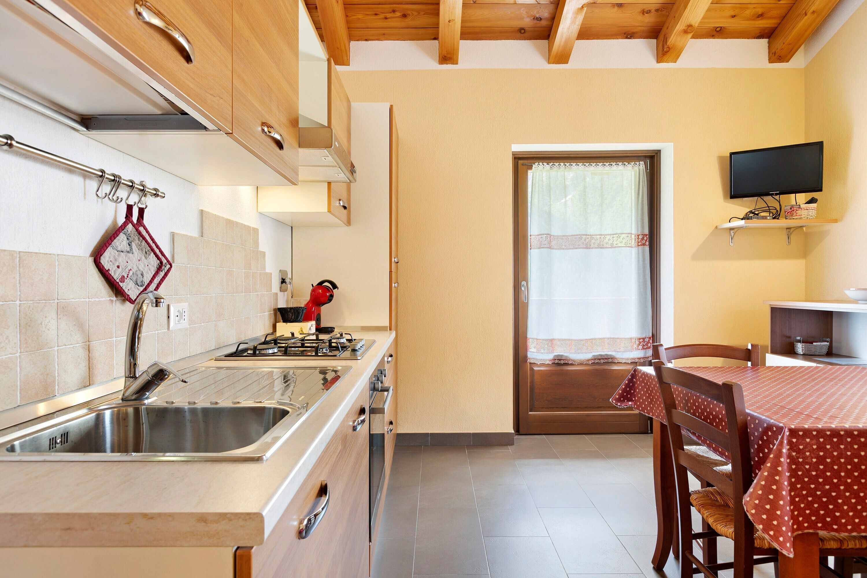 Eine Küche mit Spüle, Herd und Schränken, ein Essbereich mit Tisch und Stühlen sowie ein Fernseher an der Wand.