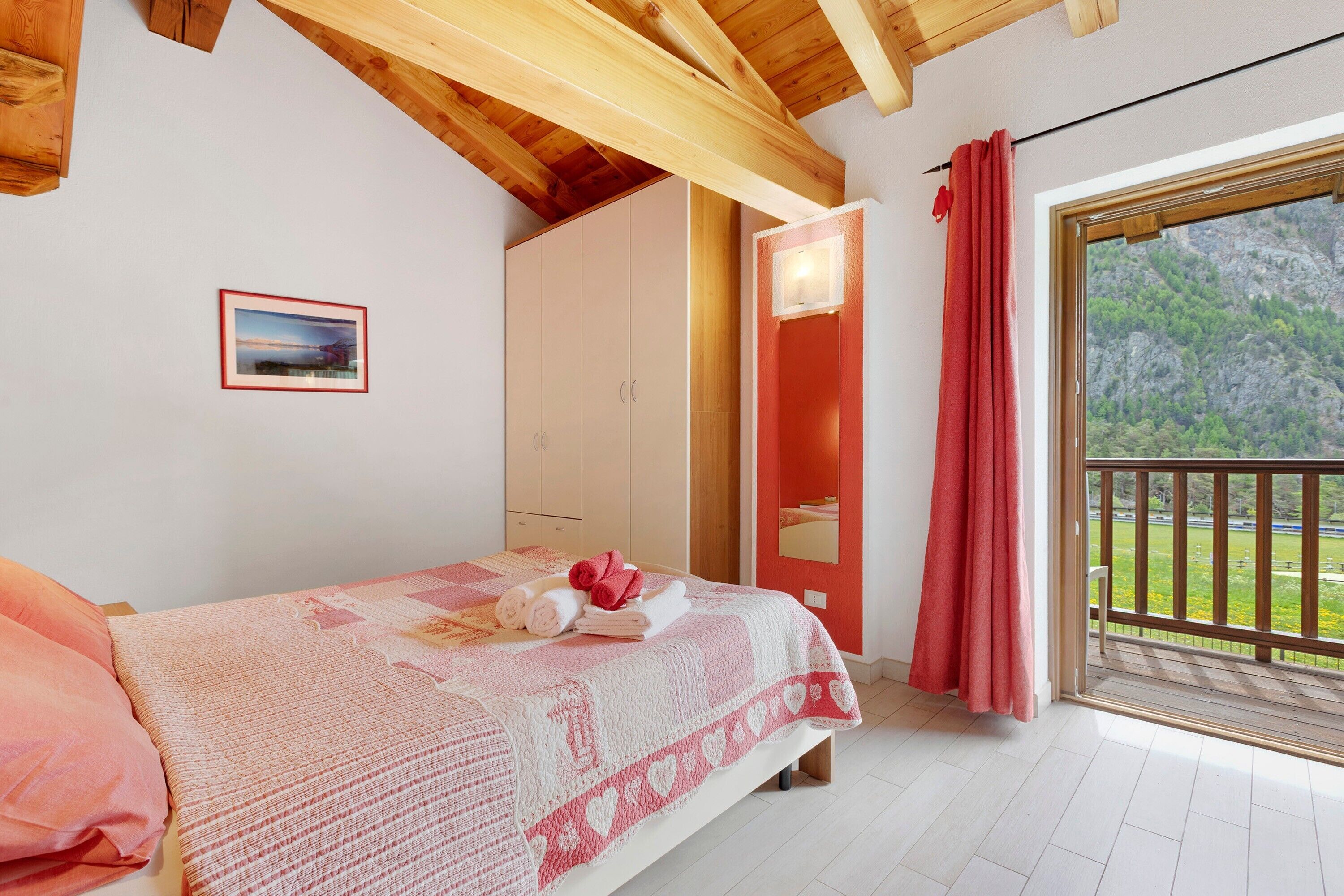 Un dormitorio con cama, ventana con vista a follaje, puerta y techo de madera.
