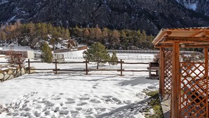 Un paisaje nevado con un porche de madera, una zona cercada y montañas al fondo.