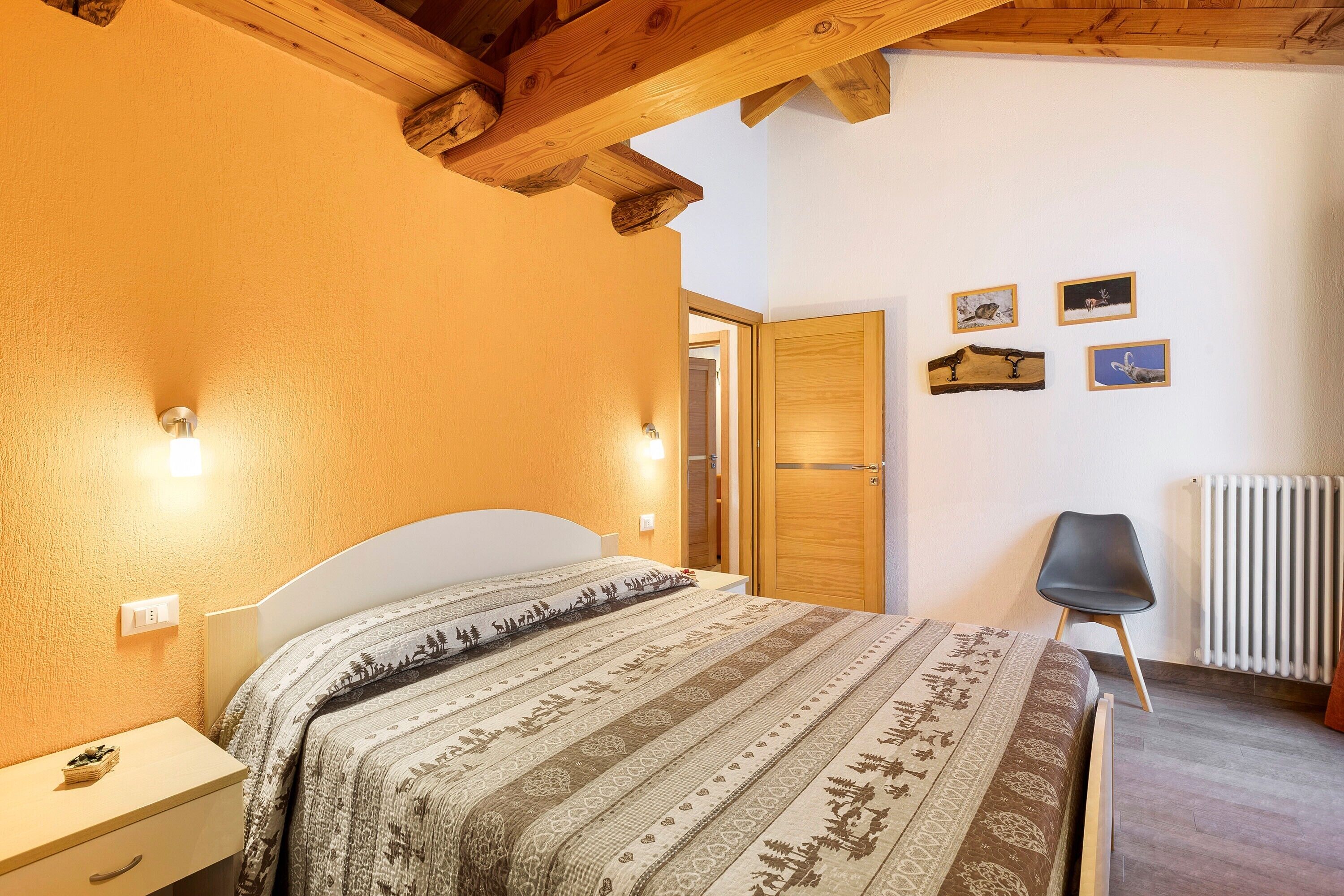 Ein Schlafzimmer mit Bett, Nachttisch, Wandleuchte, Holzbalkendecke, Heizkörper und Stuhl.
