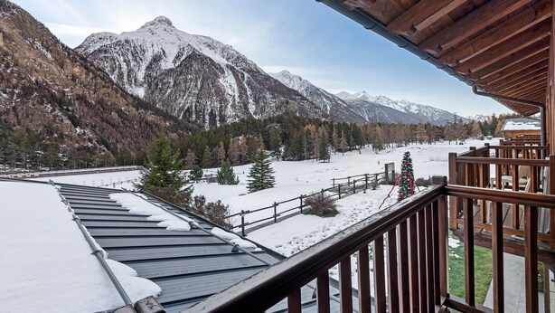 Ein Blick auf die Berge vom Holzbalkon, mit schneebedecktem Boden und Bäumen.