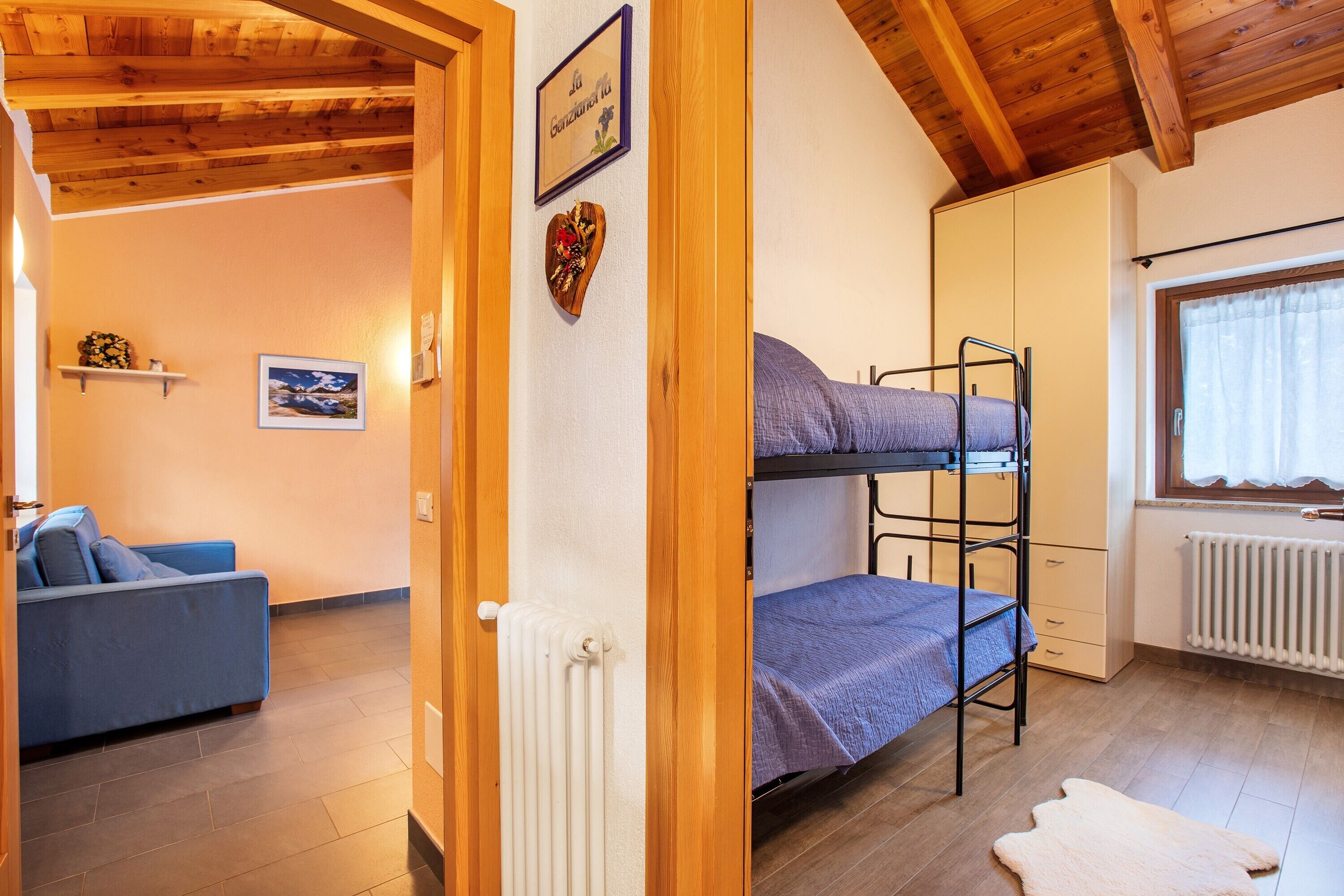 A room with a bunk bed, a sofa, a radiator, and a window with curtains.