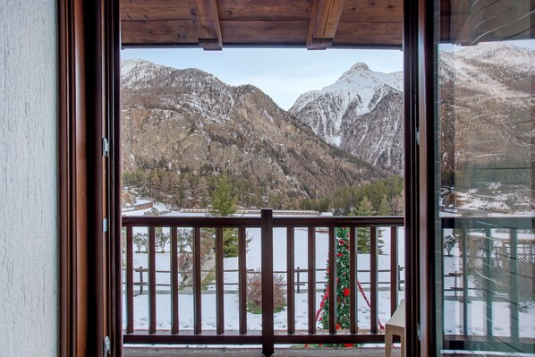 Blick durch ein Fenster mit einem Holzbalkon und einer verschneiten Landschaft.