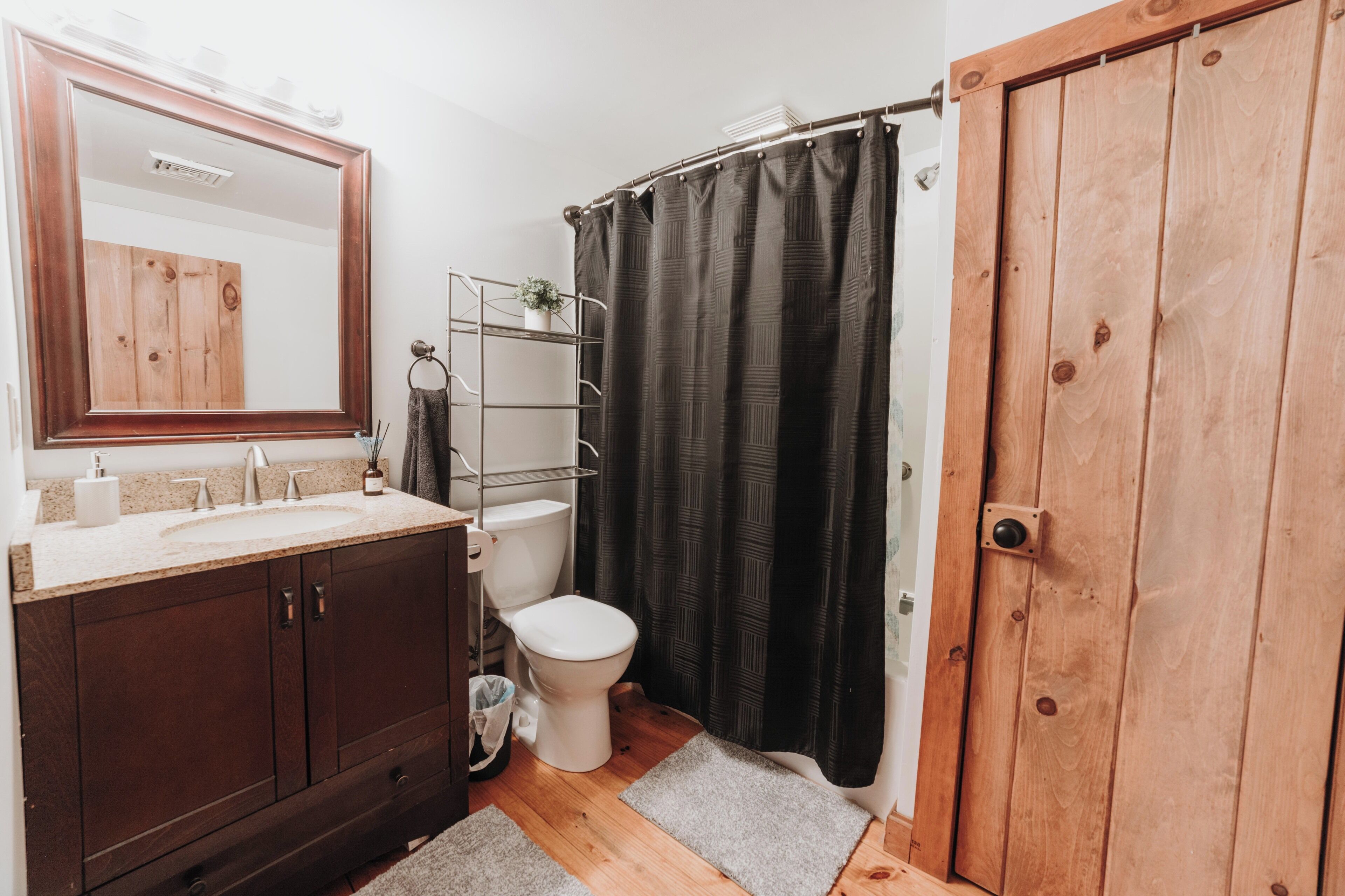 A bathroom with a wooden vanity, a toilet, a shower curtain, and a wooden door.