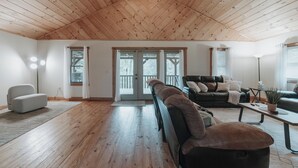 A spacious living area with wooden flooring, a high ceiling, and a large sliding glass door leading to an outdoor deck. - Cozy 3-bedroom cabin with a spacious wrap around deck located in landisburg pa (Landisburg)