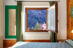 A bedroom with a wooden bed, a window with a view of a forest, and a green door. - Apartment 'L'Achillea' with Lake View and Wi-Fi (Bionaz)