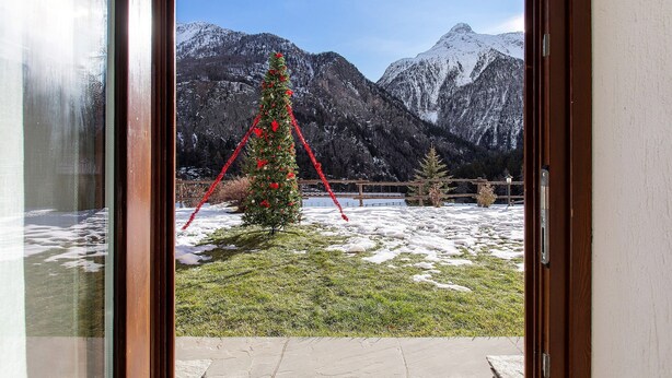 Aussicht auf Berge durch ein Fenster mit einem geschmückten Weihnachtsbaum.