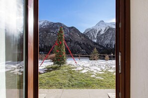 Bergzicht door een raam met een versierde kerstboom.