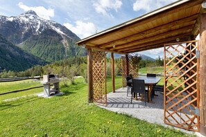 A covered outdoor seating area with a table and chairs, a grill, and a view of a mountain range. - Apartment 'L'Achillea' with Lake View and Wi-Fi (Bionaz)